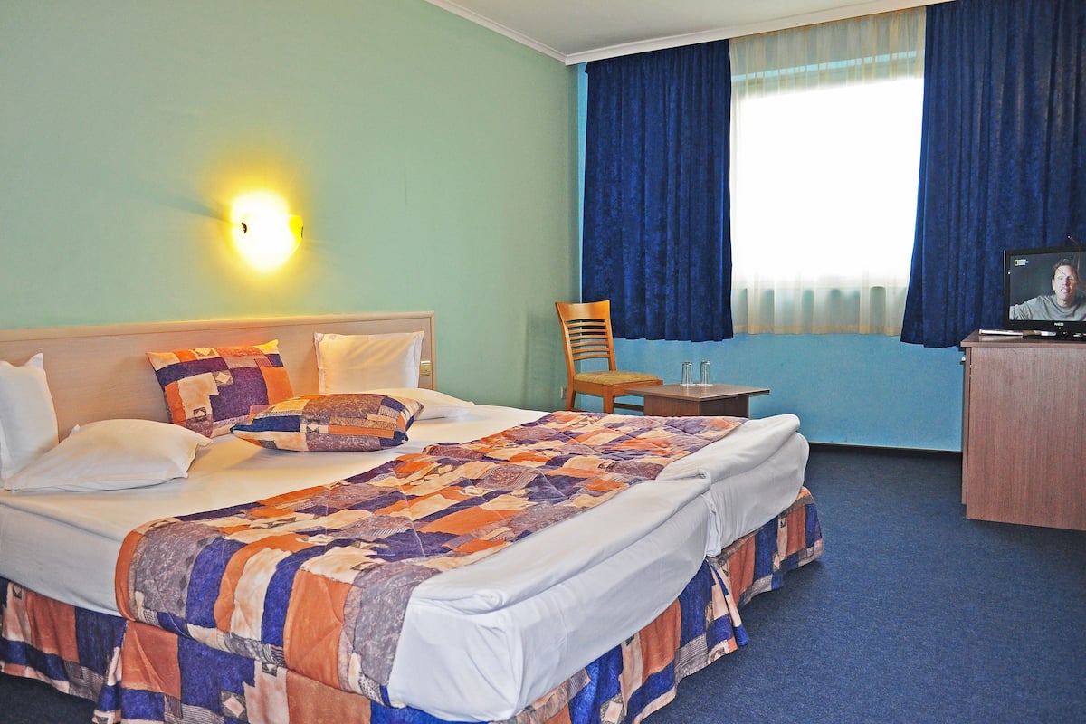 A hotel room with a large bed, a desk, a chair, and a television.