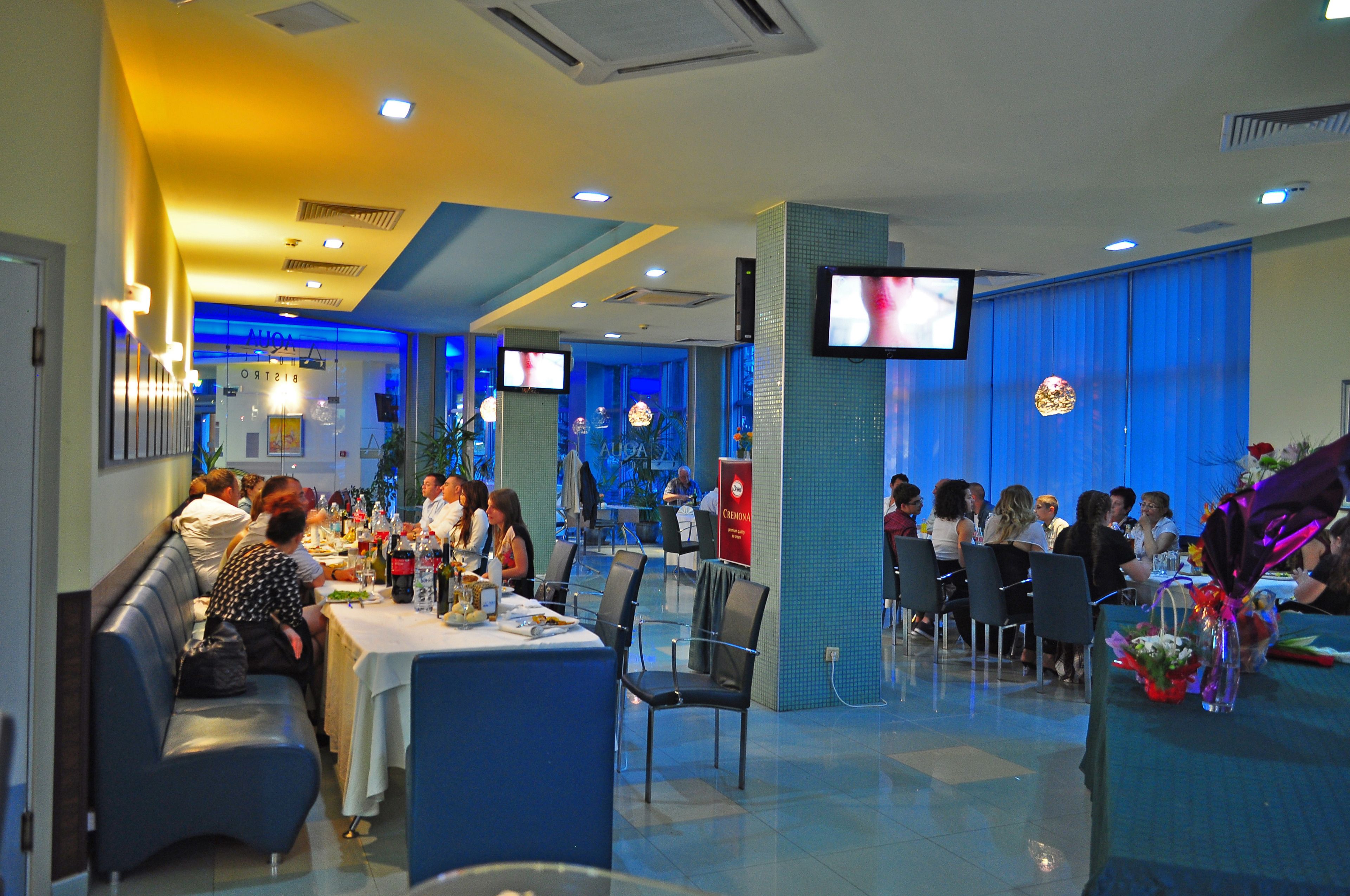 A restaurant with multiple dining tables and chairs, a television screen, and a blue-lit interior.