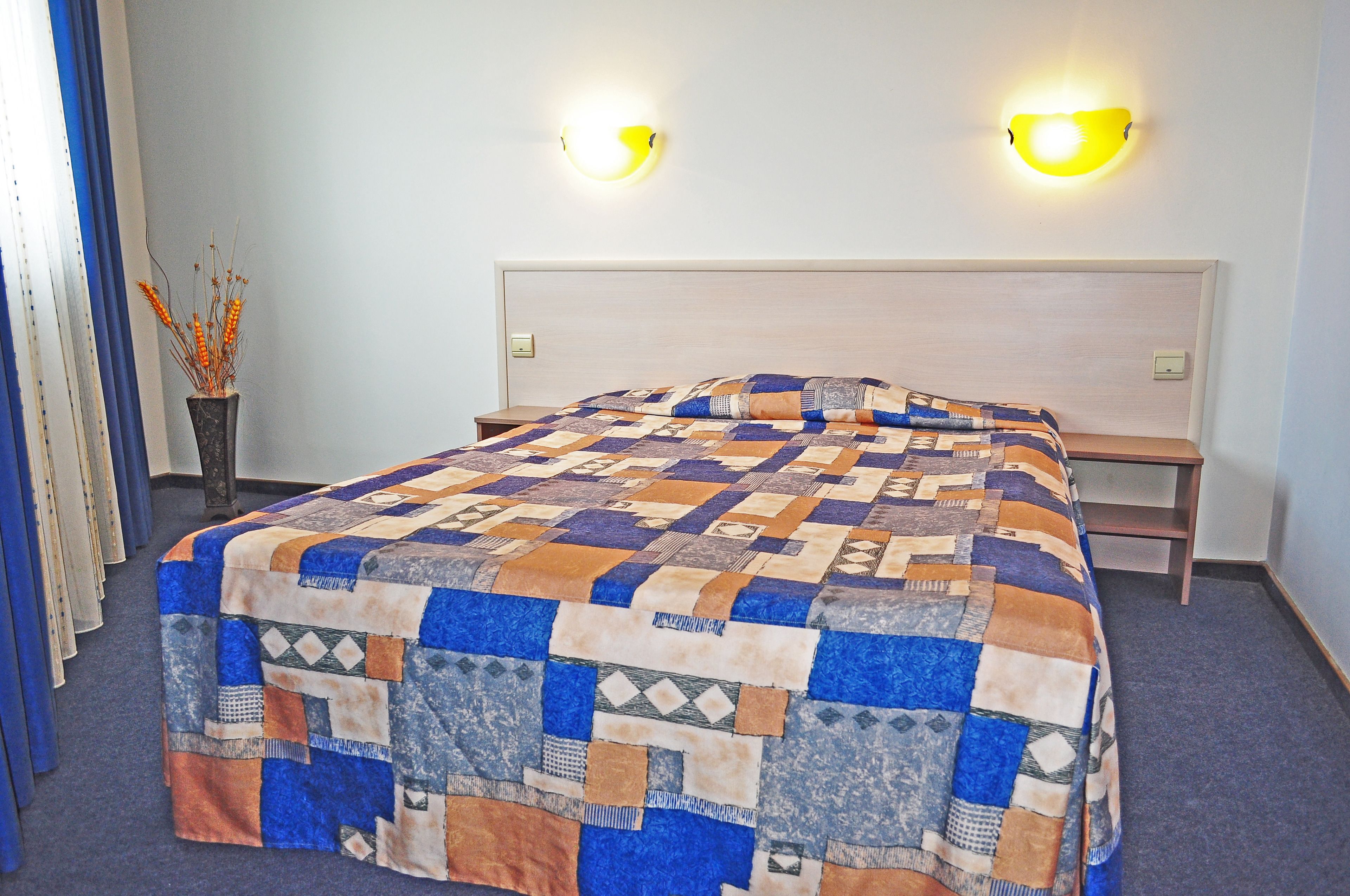 A neatly made bed with a patterned quilt, two bedside lamps, and a small table beside the bed.