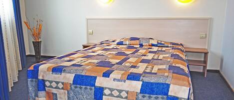 A neatly made bed with a patterned quilt, two bedside lamps, and a small table beside the bed.
