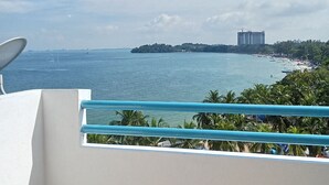 Un balcón con vista al mar, a una playa y un edificio lejano.