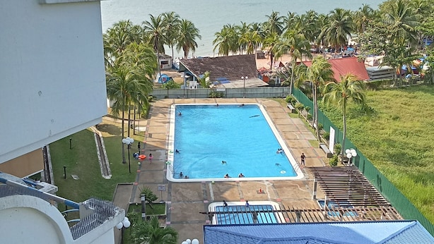 Piscina con vista al mar, rodeada de palmeras y una zona vallada.