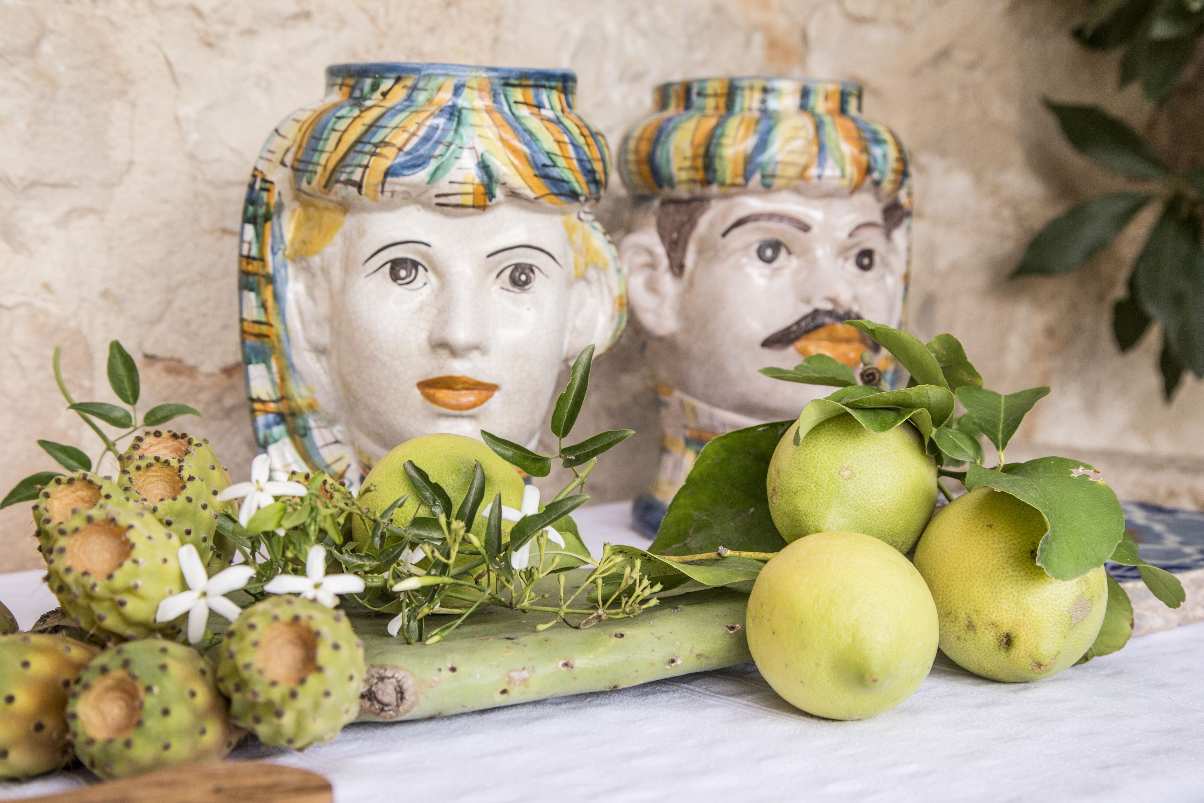 Ceramic vases with patterned lids, a cactus plant, and green fruits on a marble surface.