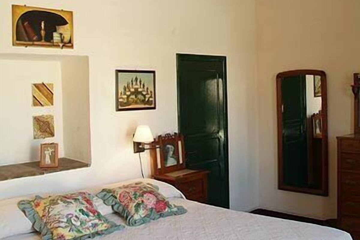 Une chambre avec un lit, un ventilateur de plafond, une porte verte et des œuvres d’art murales.