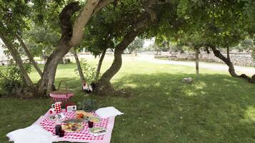 Un montaje para picnic bajo un árbol, con una manta a cuadros, comida y utensilios.