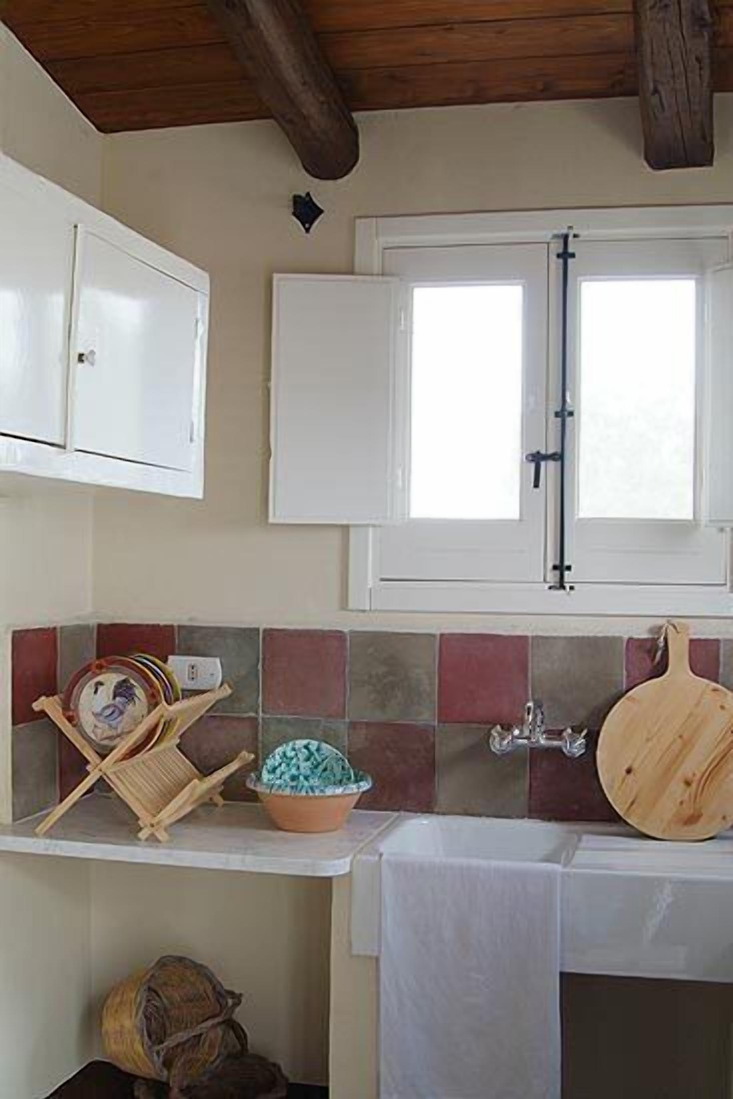 Una cocina con salpicadero de azulejos, techo de madera y ventana con marco blanco.