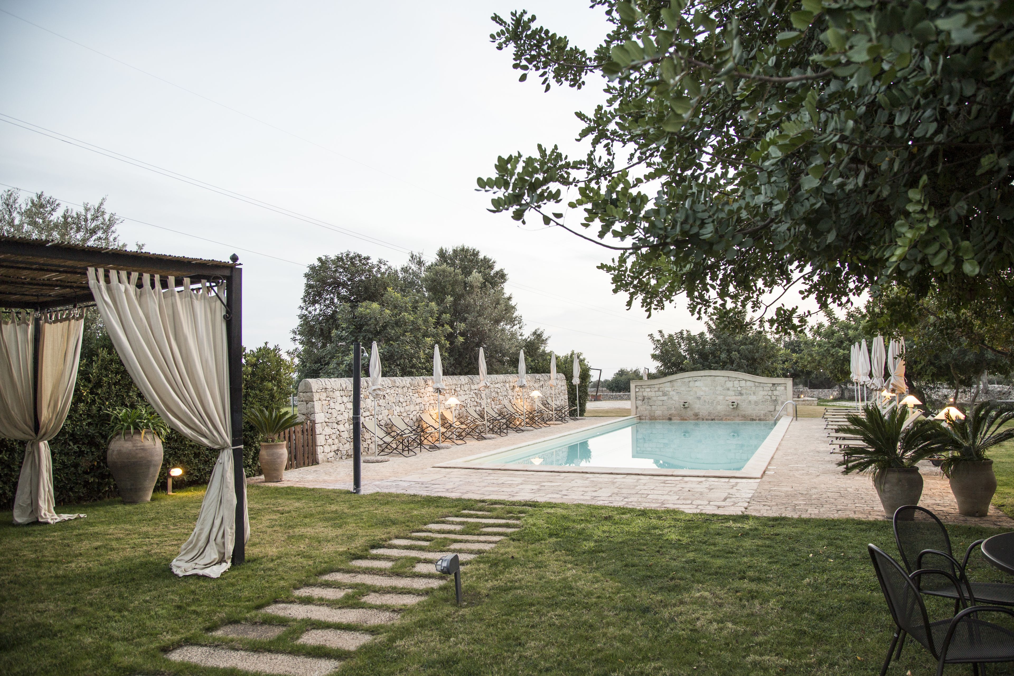Un patio trasero con piscina, muros de piedra y plantas en macetas.