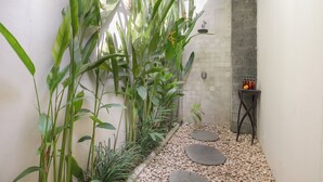 A small, enclosed garden area with a tiled wall, a stone bench, and a small table with bottles. - Villa Koala (Seminyak)