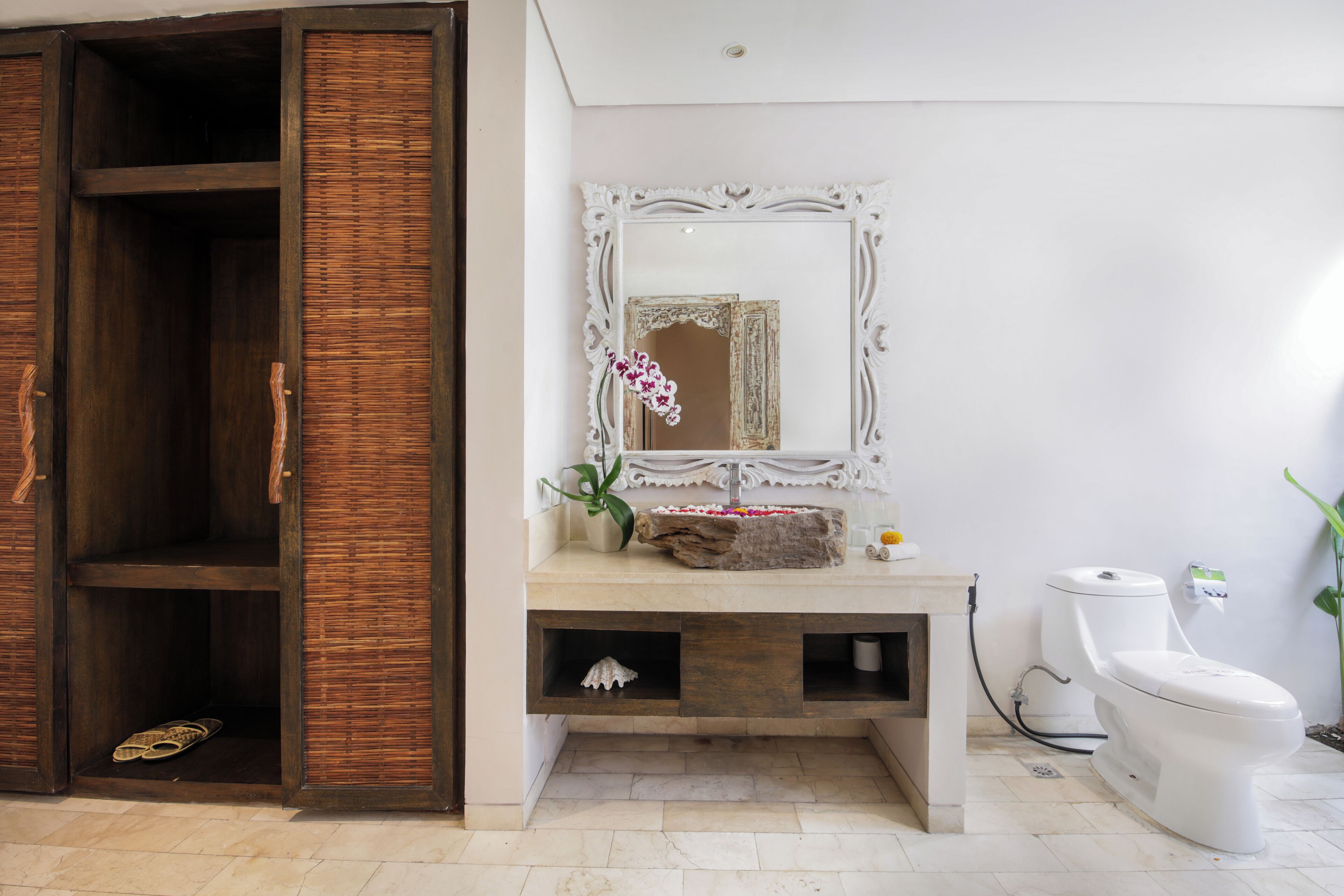 A bathroom with a wooden wardrobe, a white sink with a decorative mirror, and a toilet.