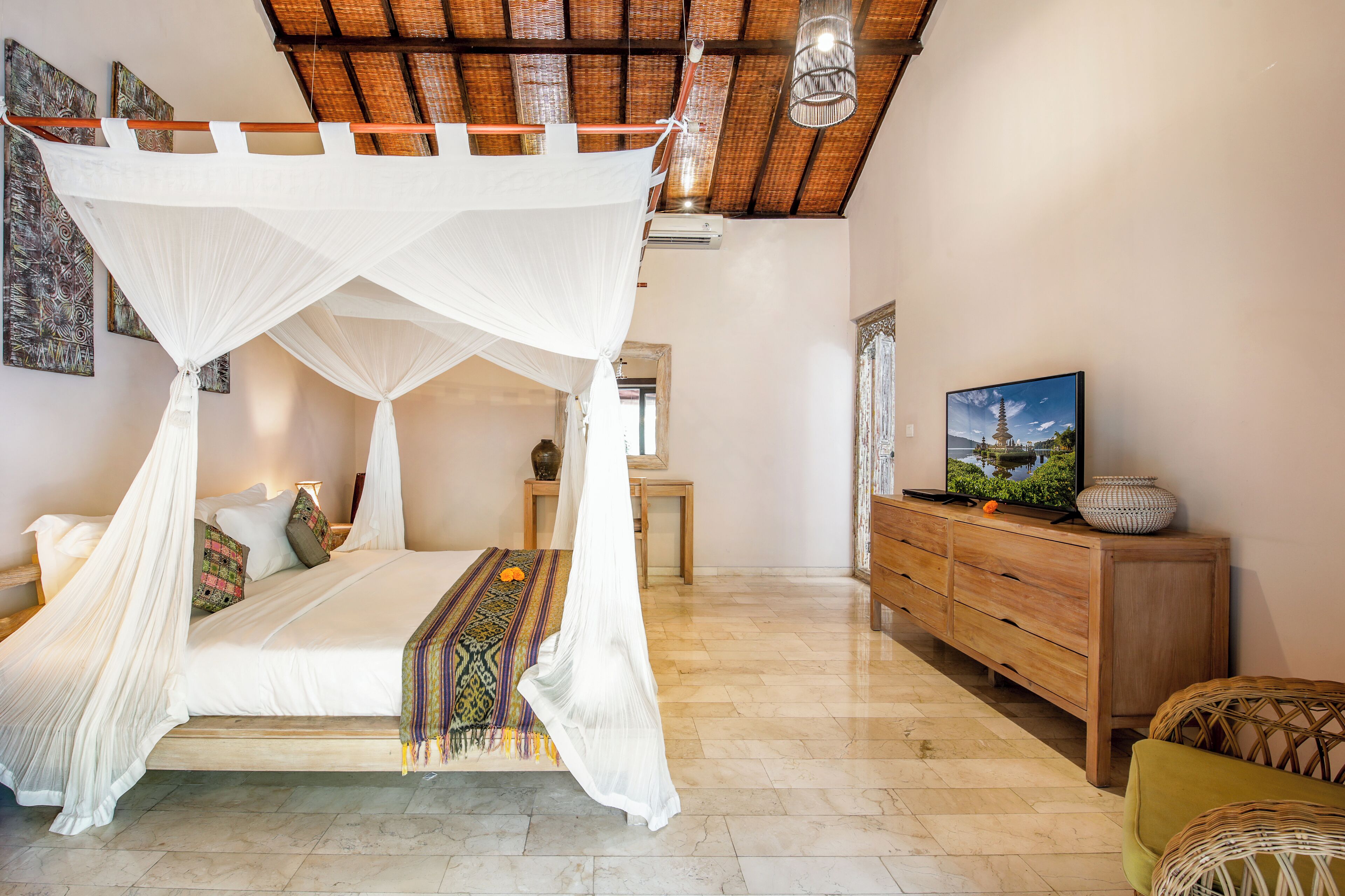 A bedroom with a four-poster bed, a wooden dresser, and a television on a cabinet.