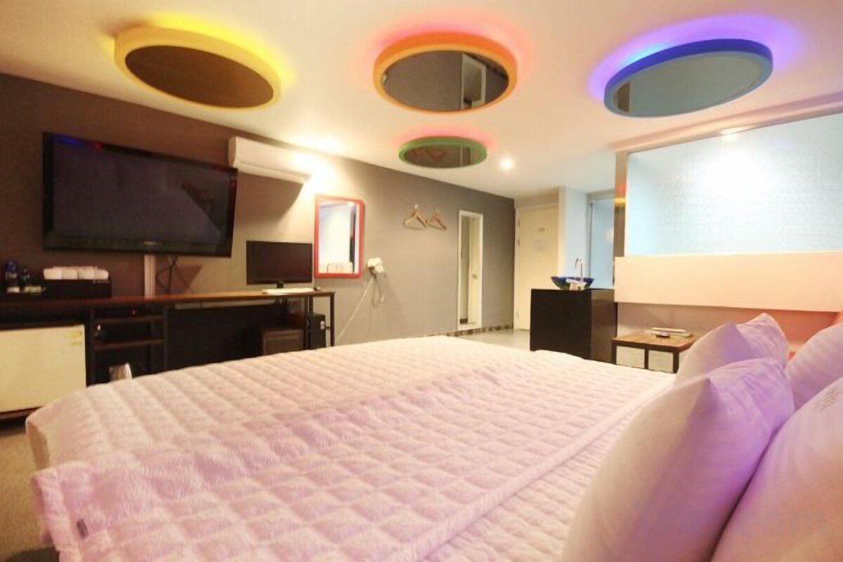 Quarto de hotel com uma cama grande, televisão de tela plana, escrivaninha e espelho.