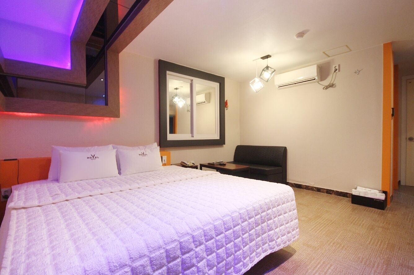 A hotel room with a large bed, a desk, a chair, and a mirror on the wall.
