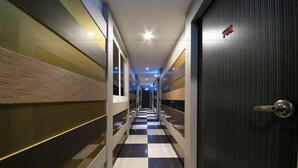 Un corridoio d'hotel con pavimento a scacchi, pareti a specchio e una porta con logo rosso.