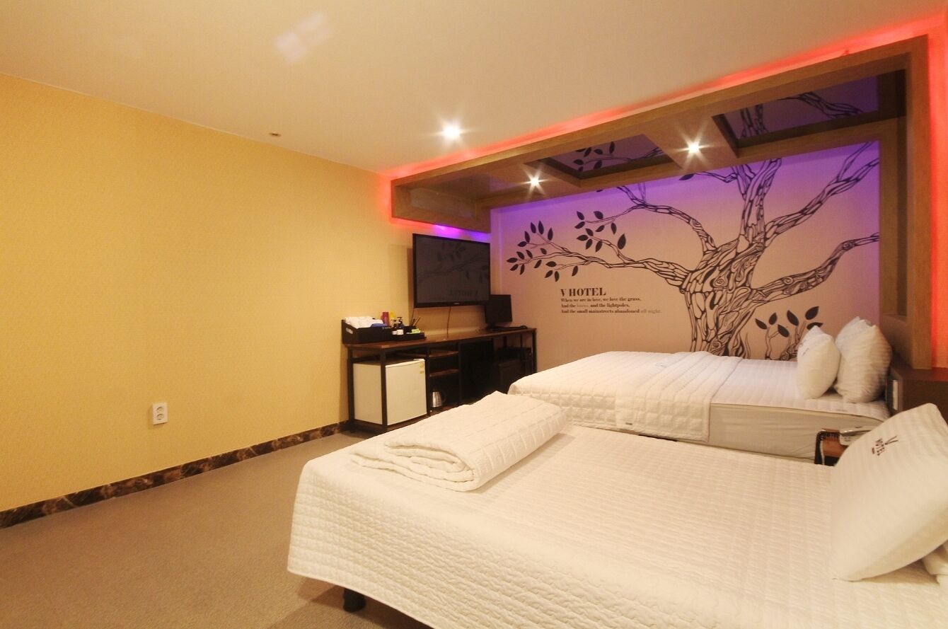 A hotel room with two beds, a desk, a television, and a wall mural.