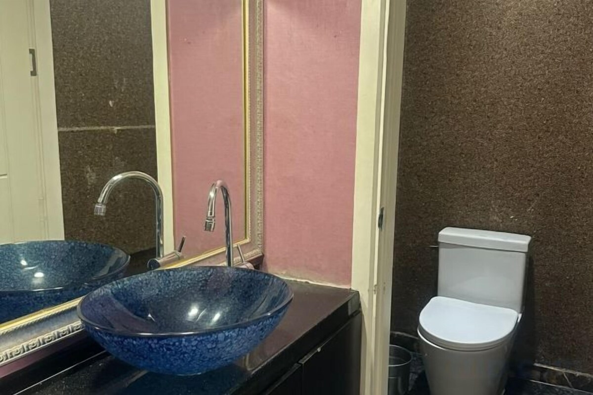 Casa de banho com duas pias de vidro azul, um espelho e uma sanita.