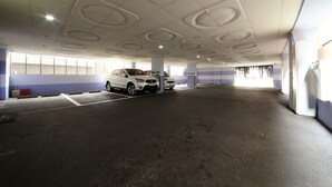 Un parcheggio multipiano con un'auto bianca al centro. Il soffitto presenta motivi circolari e ci sono finestre lungo le pareti.