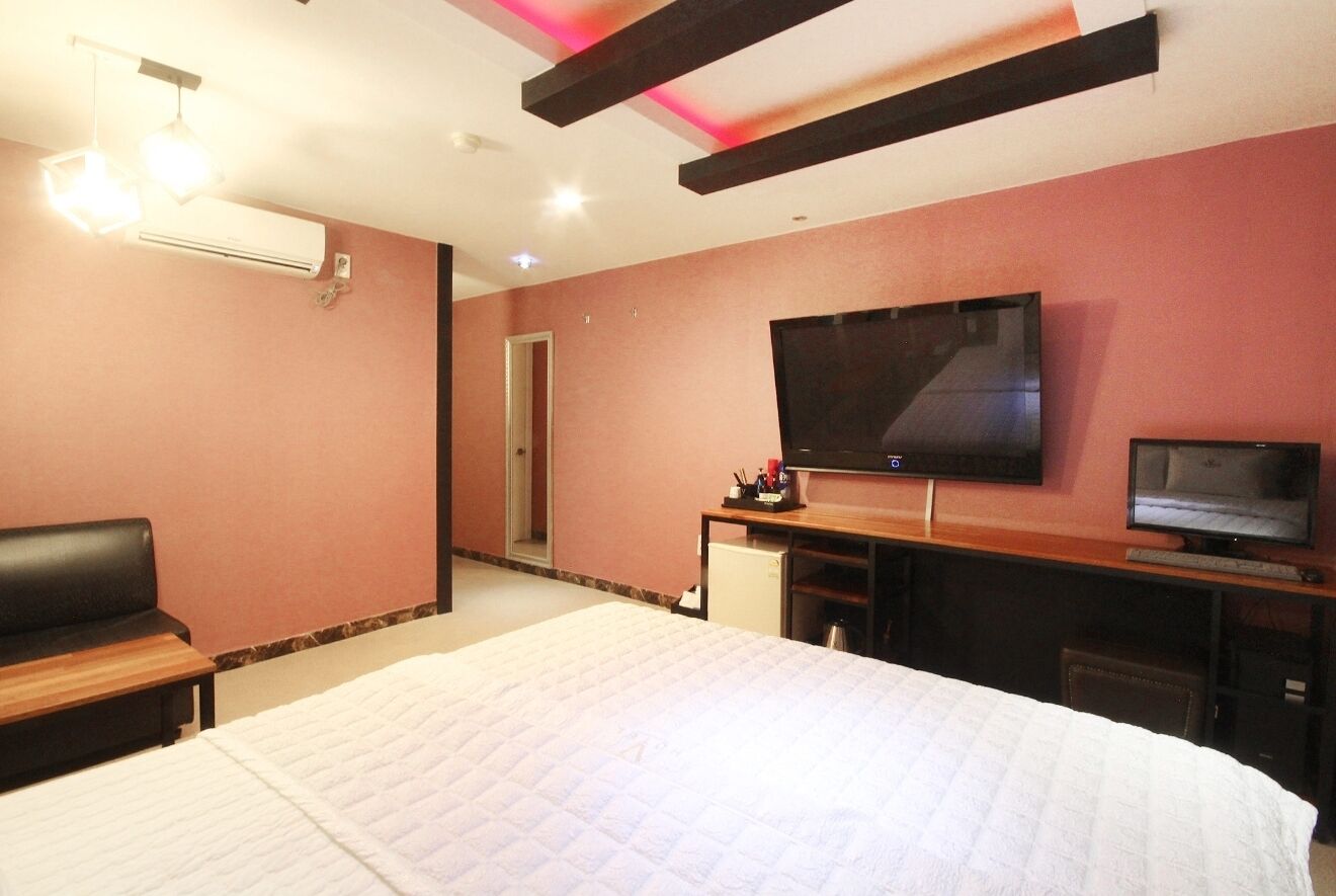 Habitación de hotel con una cama grande, televisor, escritorio con computadora y refrigerador pequeño.