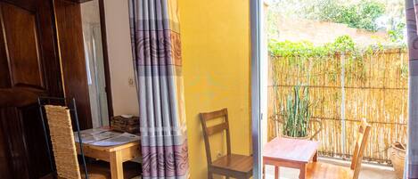 A room with a wooden table and chairs, a sliding glass door leading to a balcony with a bamboo fence and potted plants.