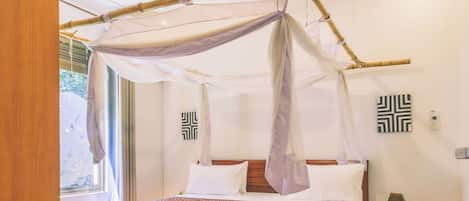 A bedroom with a four-poster bed, a nightstand, a lamp, and a view of the outdoors.