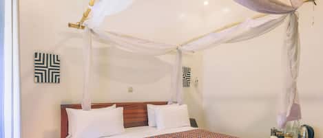 A bed with a canopy, a bedside table with a book, and a wall-mounted thermostat.