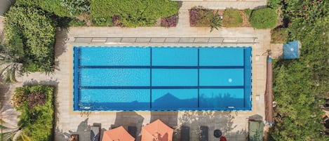 Eine Vogelperspektive auf einen rechteckigen Swimmingpool, der von Grünflächen umgeben ist, mit blauem Himmel darüber.