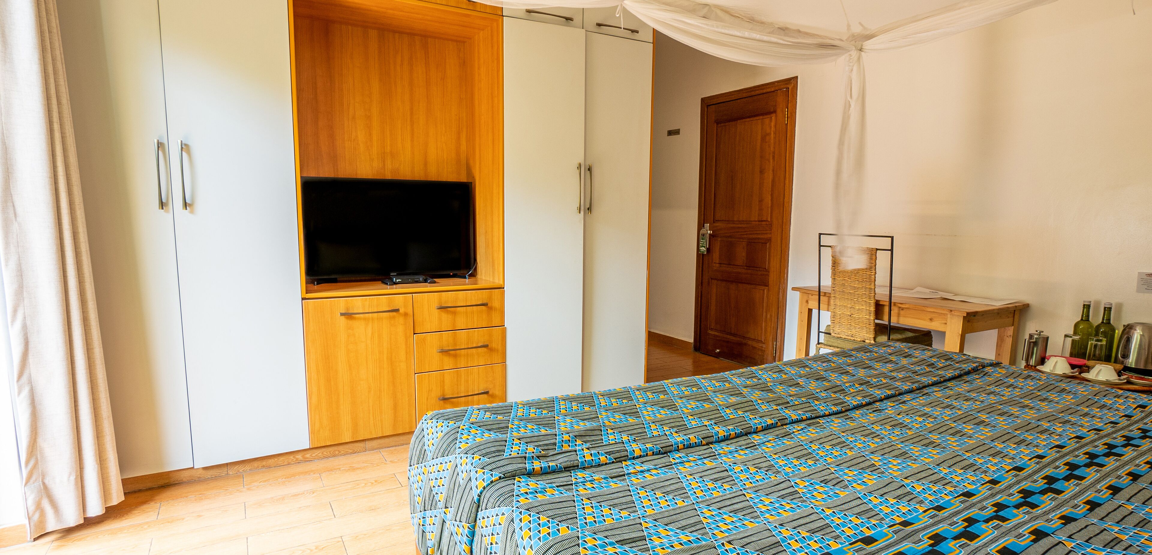 A bedroom with a bed, a wardrobe, a television, and a wooden door.