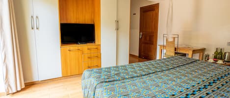 A bedroom with a bed, a wardrobe, a television, and a wooden door.