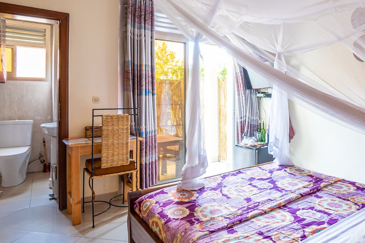 Une chambre à coucher avec un lit, une fenêtre avec des rideaux, une table de chevet et une vue sur l’extérieur.
