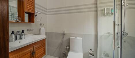 Un baño con tocador de madera, inodoro blanco, cabina de ducha con mampara de vidrio y piso cubierto de azulejos.