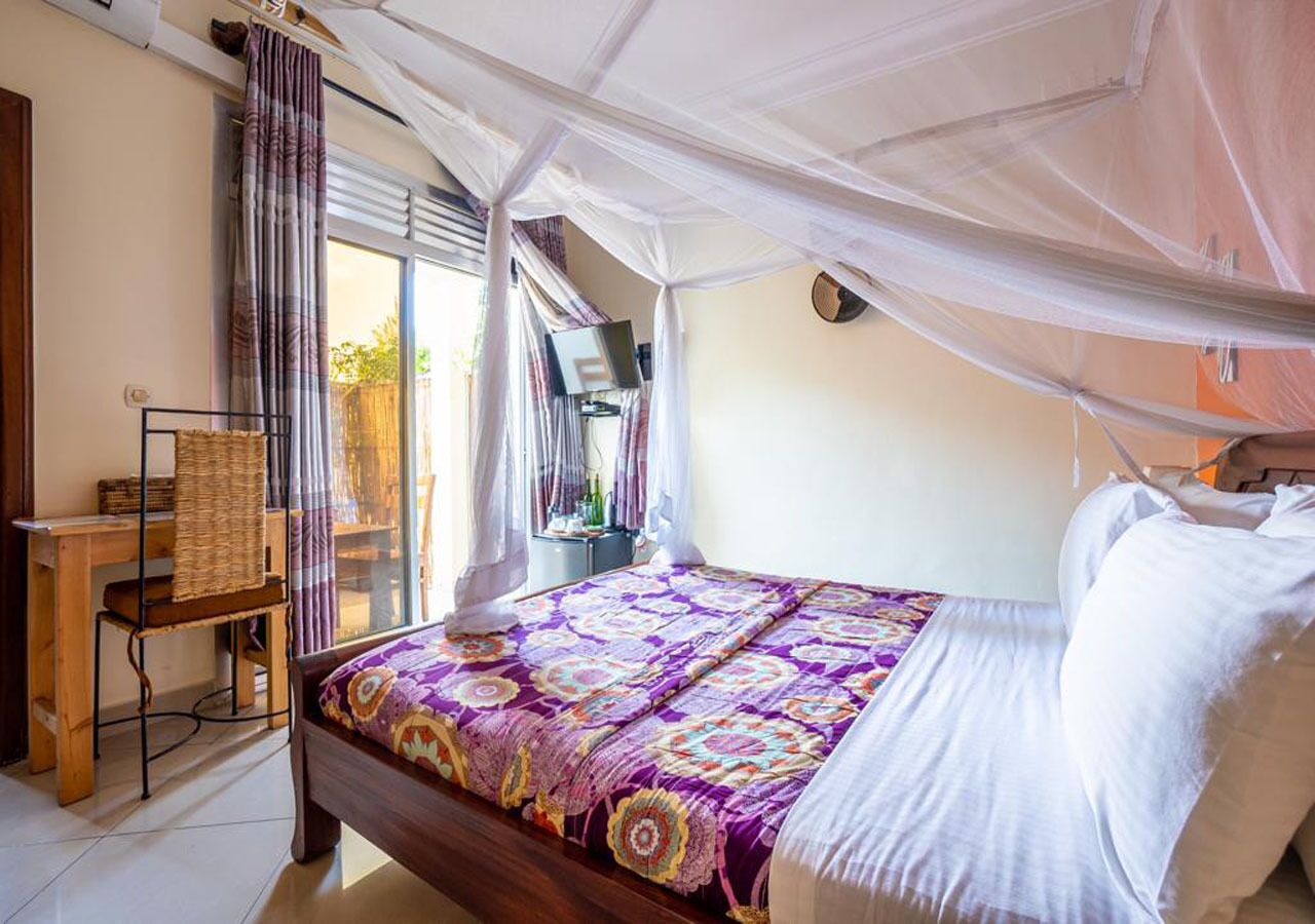 A bedroom with a bed covered in a patterned bedspread, a wooden chair, a bedside table, and a window with curtains.