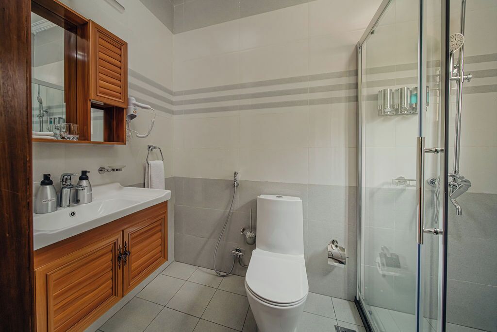 A bathroom with a wooden vanity, a toilet, a shower enclosure, and a mirror.