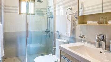 Un baño moderno con cabina de ducha de vidrio, inodoro blanco, lavabo con espejo y estante con toallas.