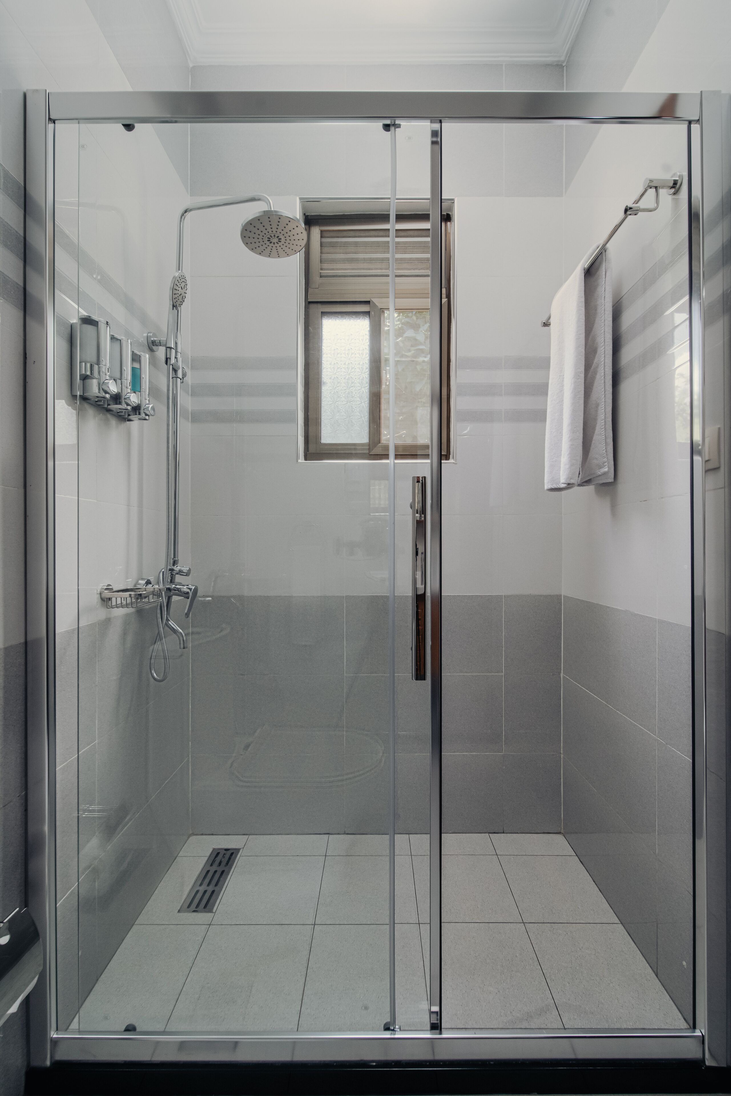 Baño con cabina de ducha de vidrio, ducha de mano, grifo empotrado y un ventanal.