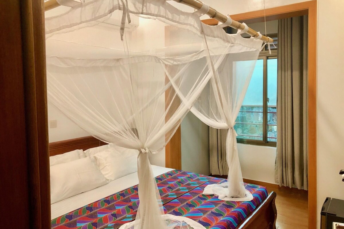 Habitación de hotel con cama, ventana con cortinas y vistas al balcón.