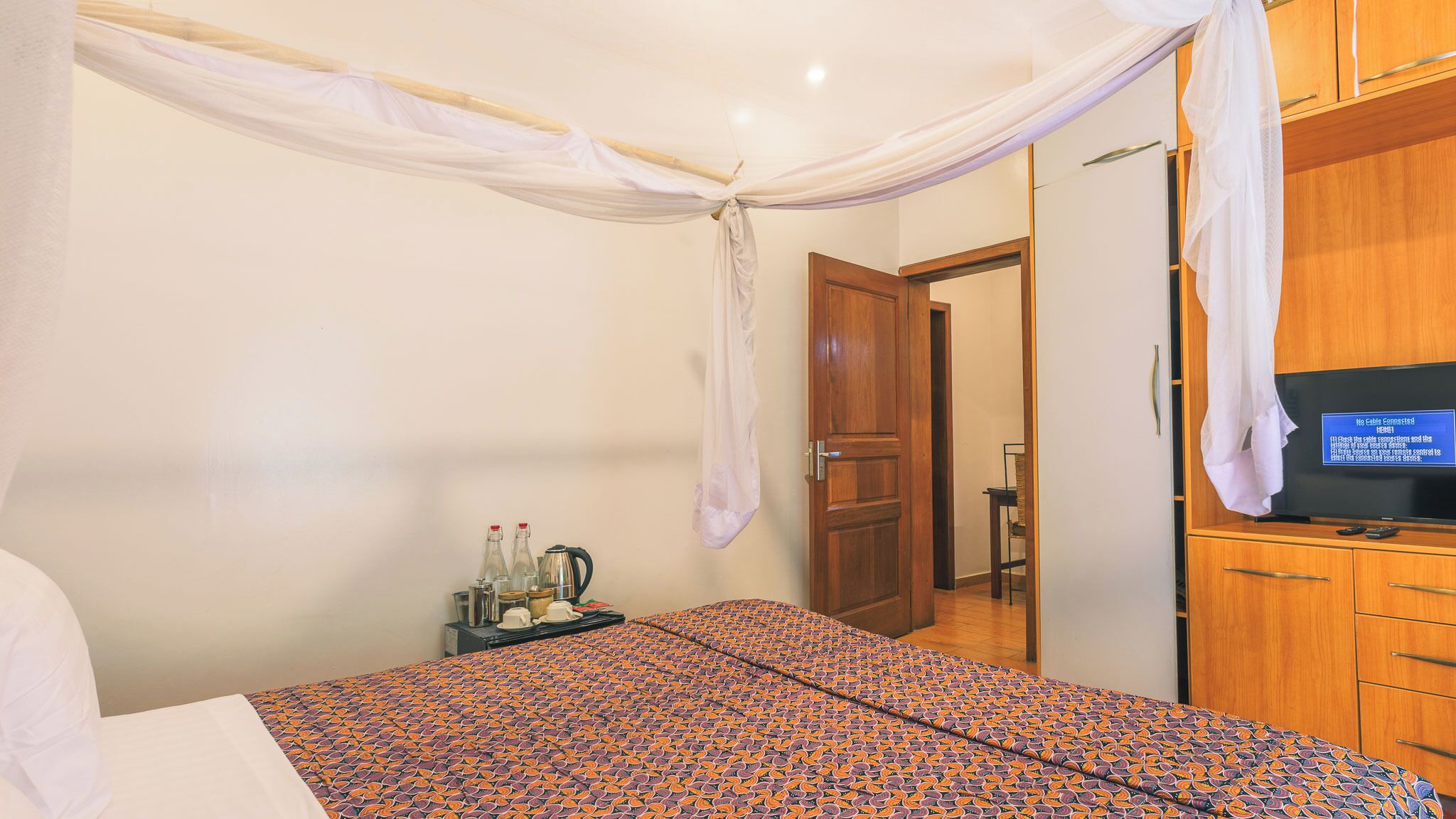 A bedroom with a bed, a television, a wooden wardrobe, and a door leading to another room.