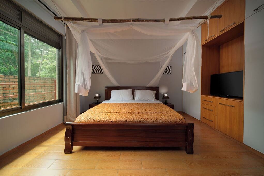 A wooden bed with a canopy, a television on a wooden cabinet, and a brick wall visible through a window.