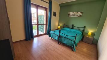 Ein Schlafzimmer mit einem Bett, einem Nachttisch, einem Fenster mit Vorhängen und Blick ins Grüne.