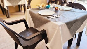 Ruokailutila, jossa on ruokailua varten katetut pöydät, tuolit ja taustalla buffetpöytä.