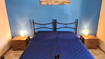 A bed with a blue quilt, two bedside tables with lamps, a wooden nightstand, and a wall-mounted picture.