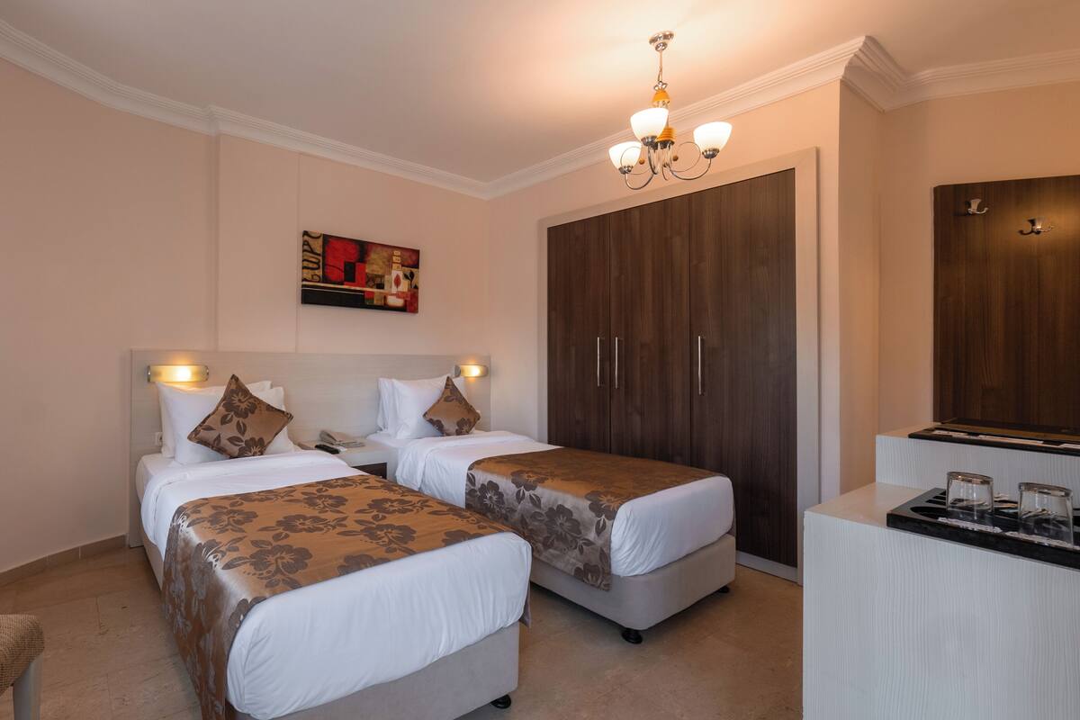 A hotel room with two single beds, a desk with a mirror, a painting on the wall, and a wardrobe.