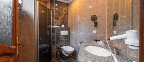 A modern bathroom with a glass shower enclosure, a granite countertop sink, and a built-in mirror.
