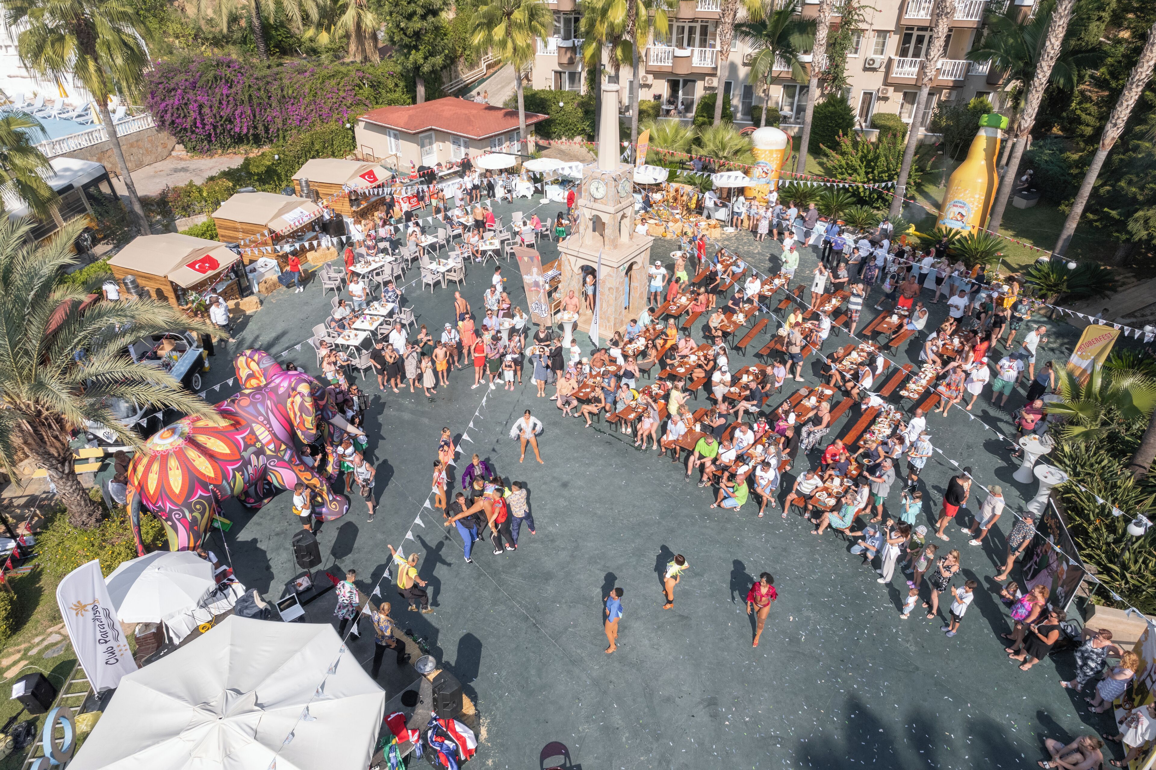 Una plaza pública al aire libre con una torre del reloj, rodeada de palmeras y diversas zonas de descanso.