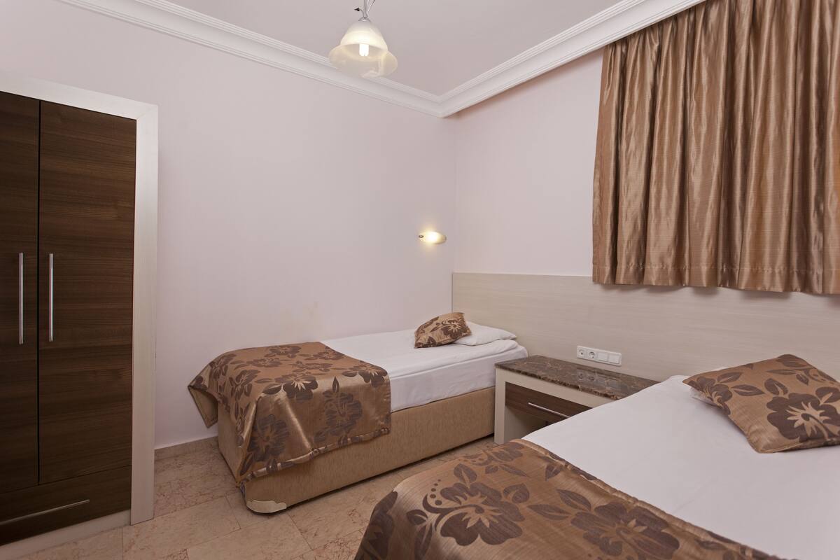 A bedroom with two beds, a wardrobe, a nightstand, and a wall-mounted light fixture.