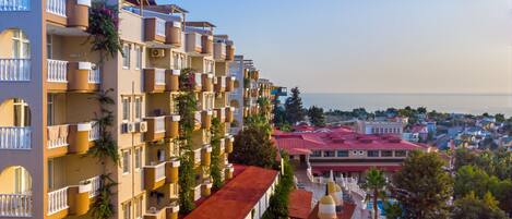 A multi-story hotel with balconies, a swimming pool, and a view of the sea.