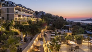 Una terraza en la azotea con mobiliario exterior, una escalera y vistas al mar al atardecer.