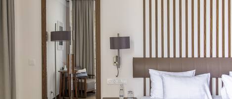 A hotel room with a bed, bedside lamps, a nightstand, a mirror, and a view of the hallway.