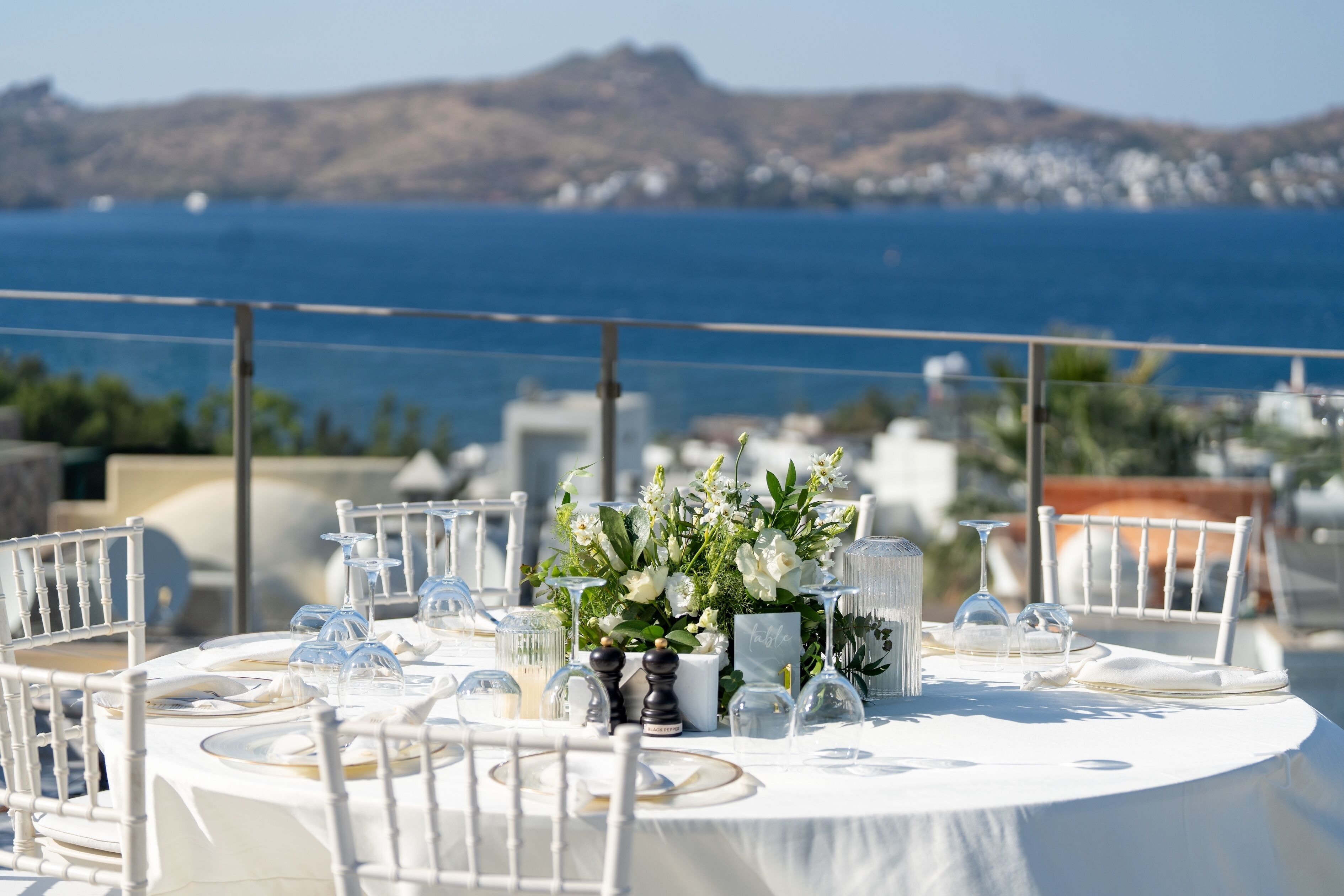 A table set for a meal with a view of the sea and mountains in the background.