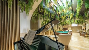 Un piano de cola con partituras, una mesa de billar y un área de descanso con sillones y mesas.