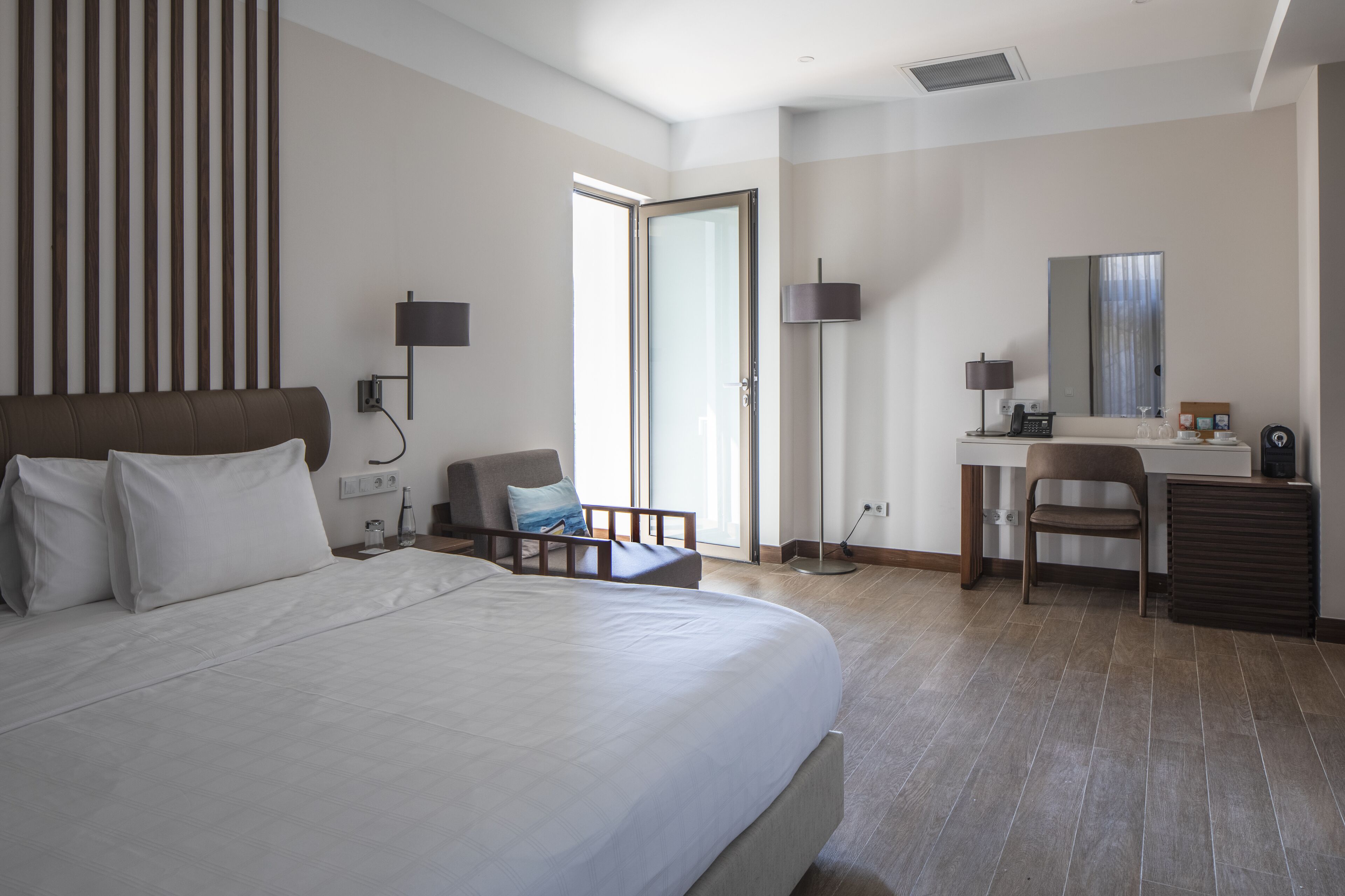 A modern hotel room with a large bed, a desk, a chair, and a wardrobe.