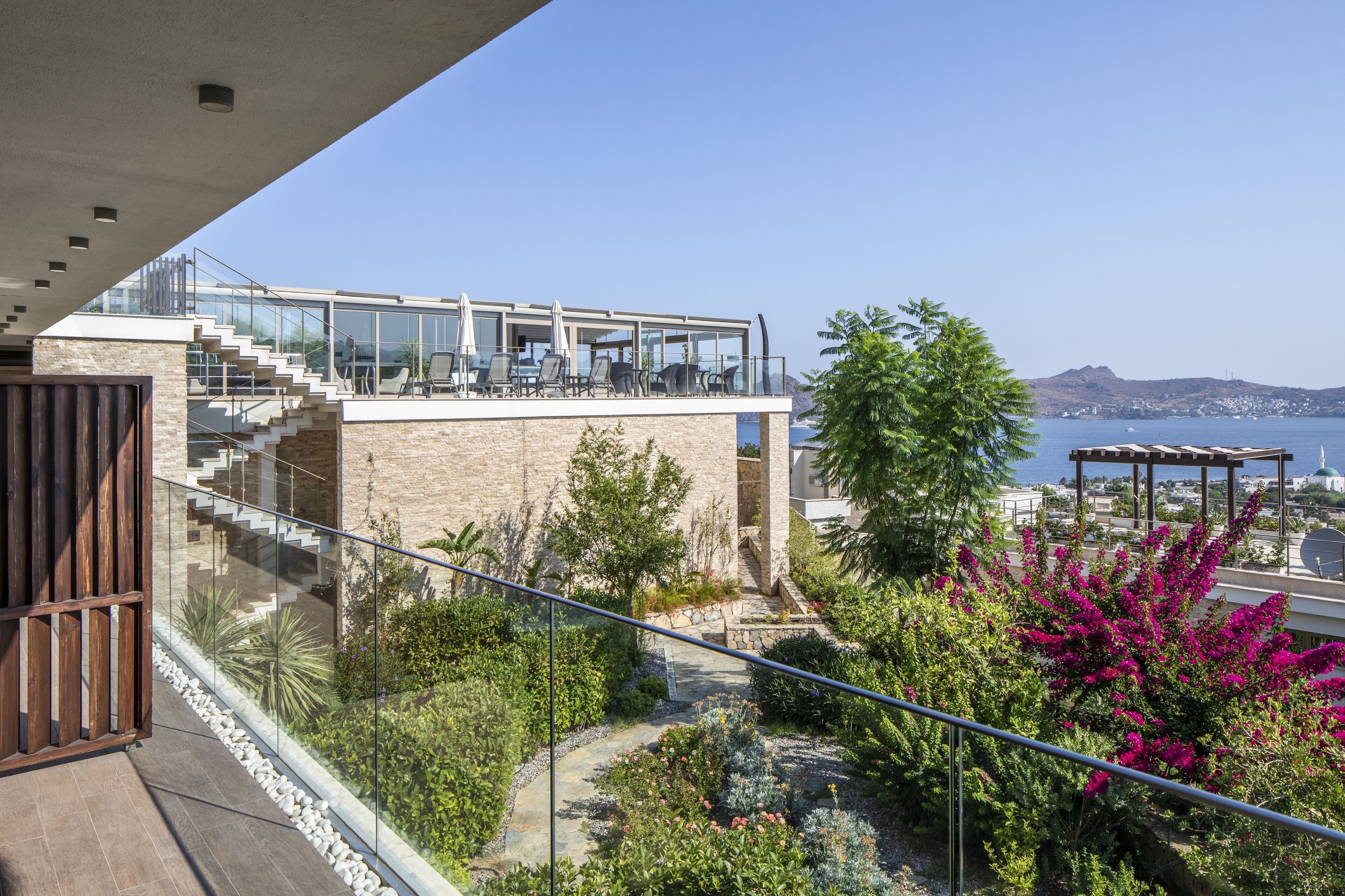 Un edificio moderno con balcón de cristal que da a un jardín ajardinado y vistas al mar.